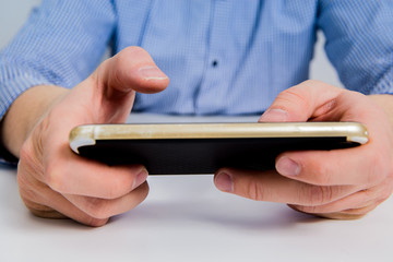 A businessman dressed in a blue checkered shirt holds a phone in his hand, writing on a mobile phone. The concept of using a smartphone to handle things.
