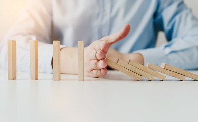 Businessman hand Stopping Falling wooden Dominoes for business solution effect from continuous toppled or risk, strategy and successful intervention. Concept of prosperity in business.