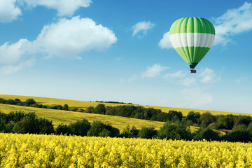 Fototapeta na wymiar Green balloon under yellow rape field on blue sky background. Landscape photography