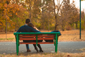 Young sweet couple embrace on a bench in park watching a beautiful sunset, enjoying their love and nature.