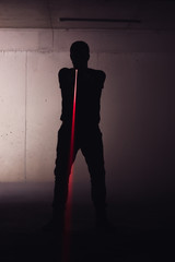 Obraz premium Silhouette of an armed man holding his gun and pointing with his laser beam at a target.