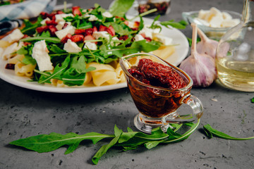 Dish with Arugula on a white plate. Green, fresh arugula on a plate, with white cheese and pasta on a stone countertop. The concept of preparing a fresh and healthy salad. Caring for health.