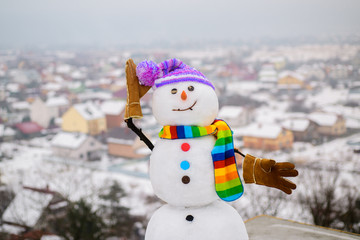 Fototapeta premium Smiling snowman on sunny winter day. Happy winter concept. Snow man in scarf, hat&mittens. Christmas card with lovely snowman. New year snowman in knitted hat&striped scarf. Happy holiday&celebration.