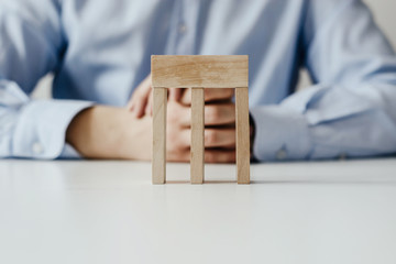 A building composed of empty wooden blocks laid by a man dressed in a business shirt. Concept of creative building. Slightly de-focused and close-up shot. Copy space.
