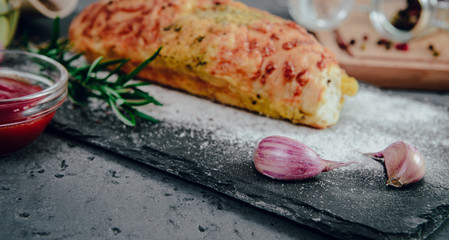 On the stone countertop lies a clove of garlic next to freshly baked bread roll with herbs. The...