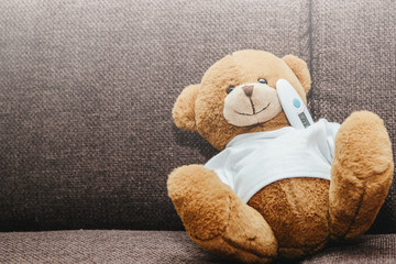 A small plush teddy bear measures a fever with an electronic thermometer. Medicine and health...