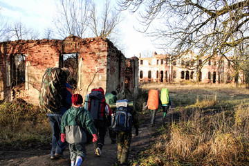 Fototapeta premium A group of hikers enjoy the last of the fall colors on a sunny day hike along a woodland trail with destroyed building ahead