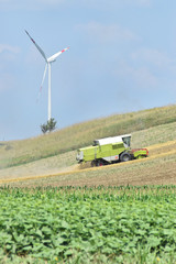 Combine harvester working in a farmland, wind farm in background        