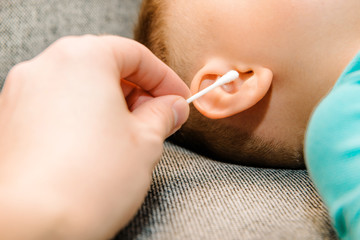 A parent cleaning the ears of a small child. Hearing problems in children, clogged ears. The parent...
