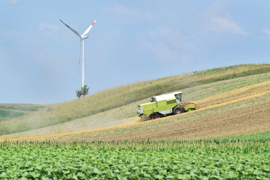 Combine harvester working in a farmland, wind farm in background        