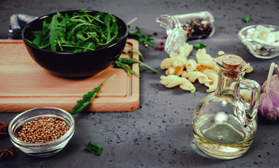Preparing and serving salads. The concept of eating and preparing meals. On the table, a bowl of rocket salad and ingredients for making a rocket salad. Spices, garlic and pasta.