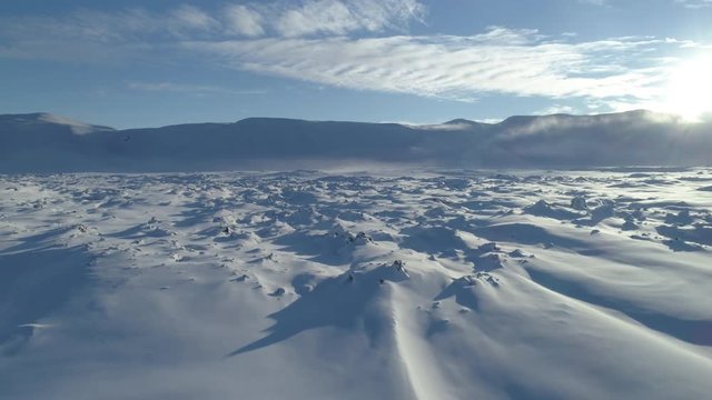 Aerial flying low over snowy lava field toward mountains and sun Iceland.mov