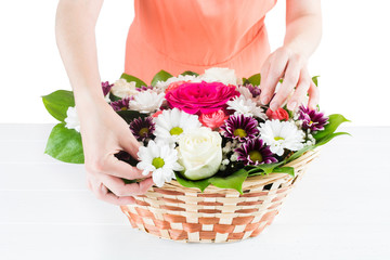 Woman florist hands composed bouquet of flowers in wicker basket on table