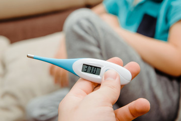 The child measures the fever with an electronic thermometer. Medicine and health concept. The thermometer held in your hand indicates a fever. Illness in a child, flu, cold.