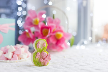 Decorative figure eight with beautiful bouquet of tender pink tulips and gift on light background with bokeh.