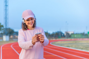 Pretty young girl doing sports on running tracks with pink cap and sweatshirt