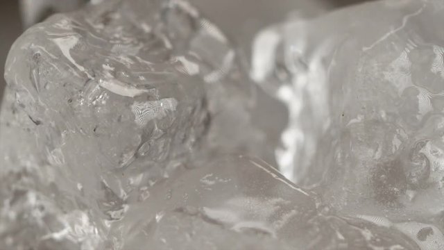 SLOW MOTION, MACRO, DOF: Detailed shot of cold water being poured over the ice cubes. Colorless transparent liquid flowing over the melting squares of ice. Warm water splashing over the ice cubes.