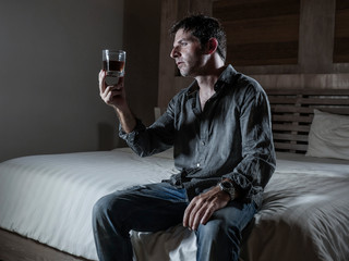 young messy and wasted drunk man drinking whiskey glass at home sitting on bed hammered and dizzy...