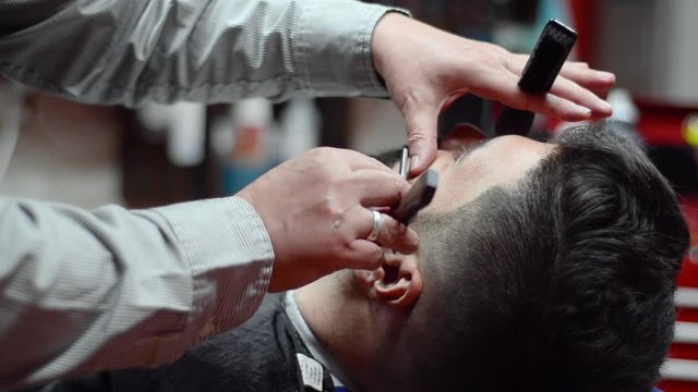 Handsome man having a shave with vintage razor at the barbershop .