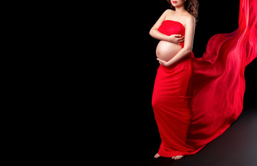 Pregnant woman in red flying  chiffon fabric holds hands on belly on a dark background. Healthy pregnancy, maternity, preparation and expectation concept. Сopy space.  Beautiful photo of pregnancy.