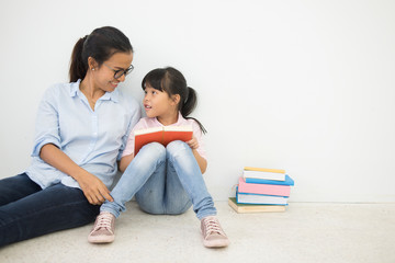 young mother and daughter sitting on floor white wall background. Adult education, Education Knowledge Concept