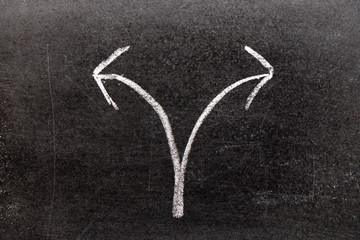 White chalk hand drawing in two way arrow shape on black board background (Concept for making decision)