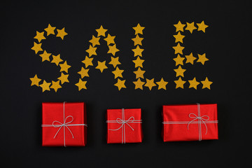 Word sale made from gold star and red gift boxes with presents on black background. Flat lay.