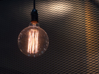 Tungsten orange light bulb hanging on the inside of the building with a black iron fence around.
