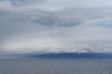 Cloudy sky with the ocean and a blue mountain silhouette 