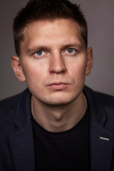 Fototapeta premium Cute serious young man in a jacket, close-up, gray background