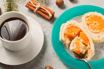 Sweet roll with whipped cream and tangerine filling and Christmas decorations and a cup of coffee