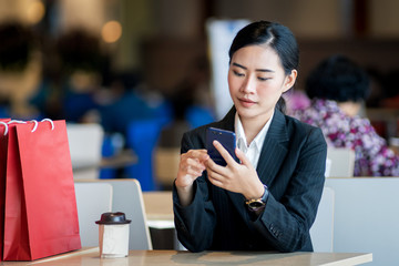 Young Asian girl sits on the chair enjoys online shoppingl. Young female purchases thing online using mobile phone, laptop, credit card.