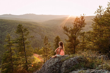 blonde woman tourist sitting on a rock in the mountains under the sunset in the summer