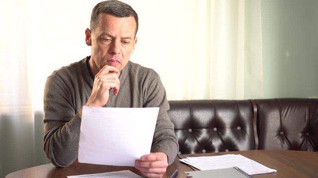 Unhappy sad man reading letter, bill, bank statement paper or tax document