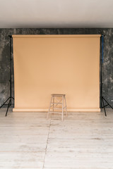 The working space of the photo studio with a beige paper background and chair.