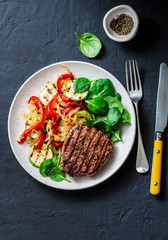 Beef steak with grilled  vegetables, sweet pepper, zucchini and fresh spinach on a dark background, top view. Delicious healthy balanced lunch