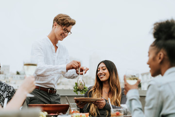Man serving his friends salad at a rooftop party