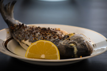 Oven baked fish Dorado with spices and a slice of lemon on a white plate.