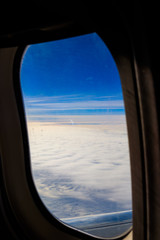 View of blue sky with white clouds through the porthole window flying airplane