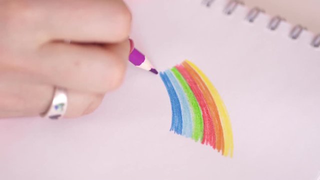 The woman draws a rainbow in a notebook. Colored pencils. Red manicure.