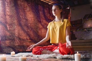 Portrait of a young girl in bright clothes practicing meditation in a crafting room surrounded by candles. Newage direction and spiritual development