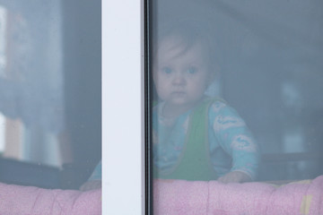 The one-year-old child looks out of the window on the falling snow.