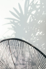Black handcraft chair with palm leaves shadow on white wall
