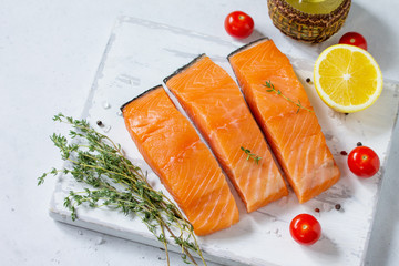 Fresh Fish. Raw Salmon Fillet, Lemon and tomatoes on a wooden board on a white stone table. Top view flat lay background. Copy space.