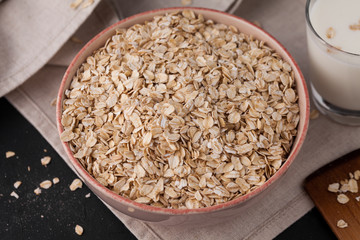 Oatmeal in a plate and a cup of milk on a towel on black background. Healthy food. close up
