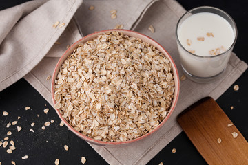  Oatmeal in a plate and a cup of milk on a towel on black background. Healthy food. close up