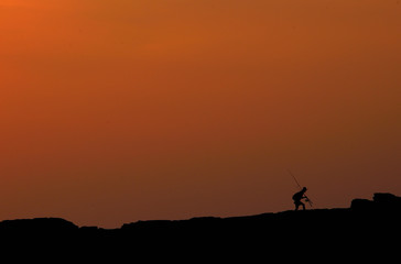 Fototapeta na wymiar Silhouette of man walking with fishing rod during sunset