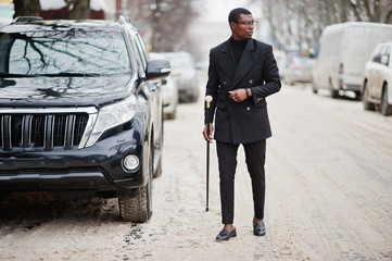 Stylish african american gentleman in elegant black jacket, holding retro walking stick with golden...