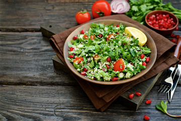 Traditional tabbouleh salad on dark brown wooden rustic background. Ingredients couscous, parsley, mint, onion, tomato. Close up view