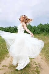 Fototapeta na wymiar Young attractive redhead bride in stylish white wedding dress spin around.